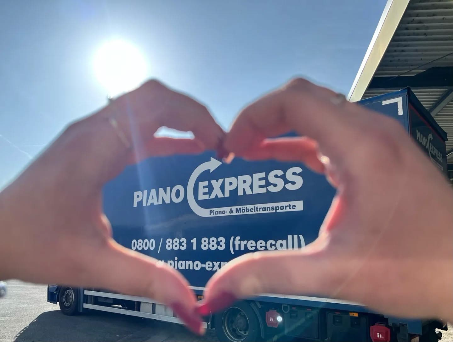 Manos formando un corazón delante de un camión de Piano-Express